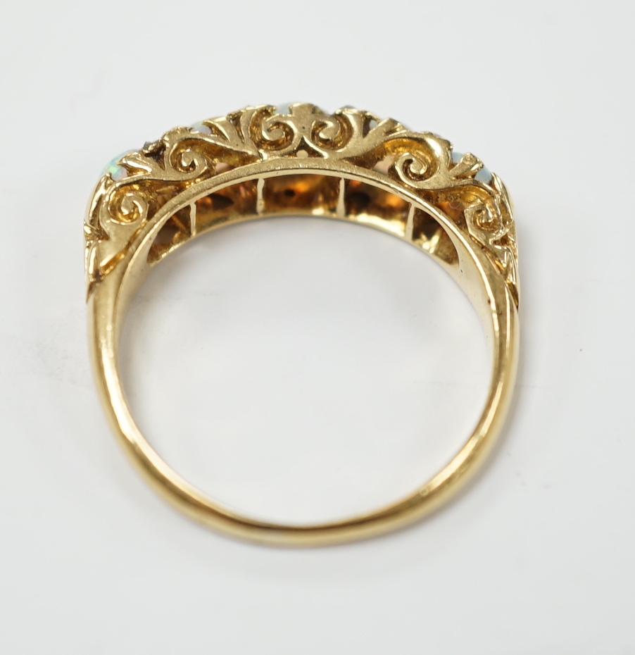 A late Victorian yellow metal and white opal five stone ring with diamond chip set spacers, size M